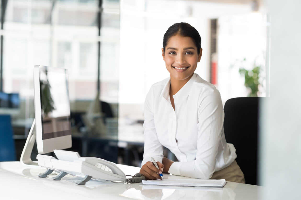 Businesswoman Sitting At Her Desk in Front of Computer and Taking Notes.