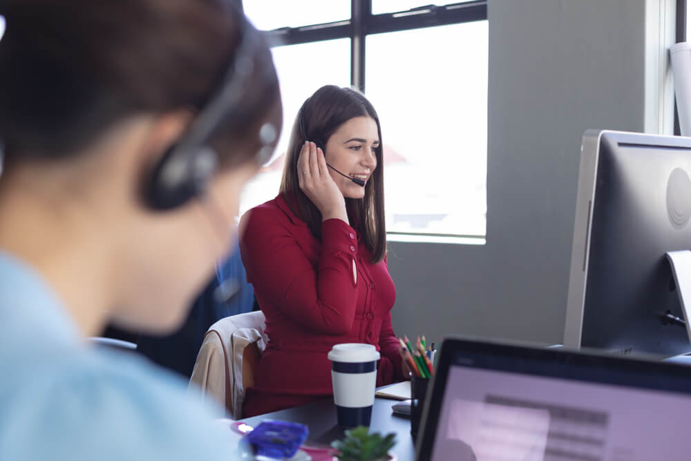 Side view of a Caucasian woman talking using a phone headset and working at a computer